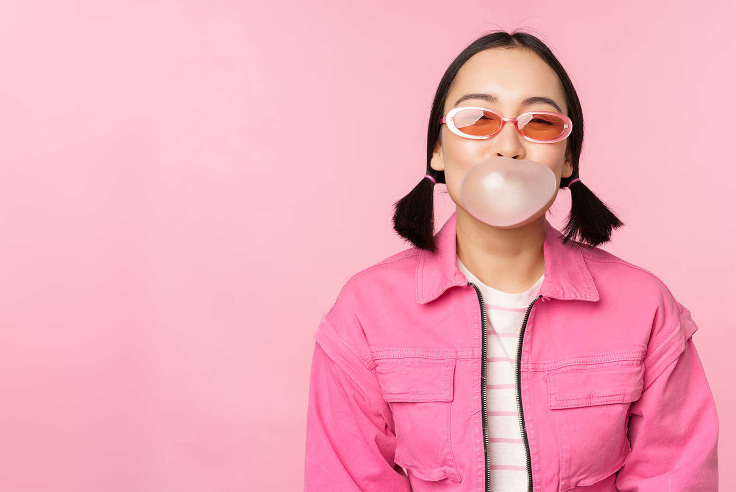 Stylisches asiatisches Mädchen macht eine Kaugummiblase mit einem pinken Kaugummi